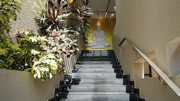 Una escalera con una estatua de Buda en la parte superior, rodeada de abundante vegetación.