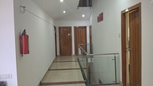 A hallway with a fire extinguisher, wooden doors, a glass railing, and a tiled floor. - VH Hotels Domlur (Bengaluru)