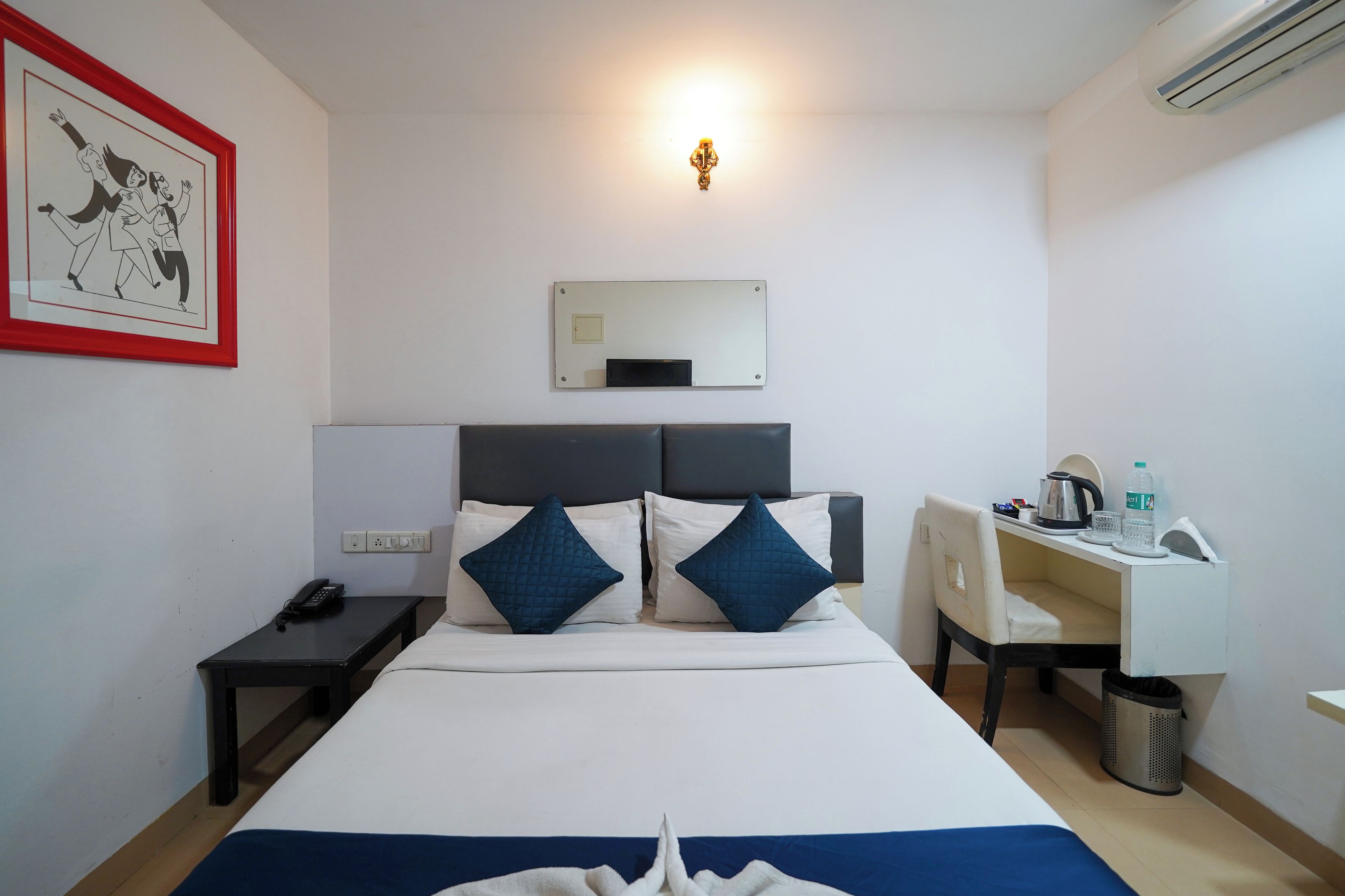 A hotel room with a bed, bedside table, desk, chair, and a wall-mounted mirror.