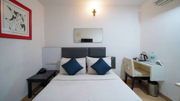 Una habitación de hotel con cama, mesita de noche, escritorio, silla y un espejo montado en la pared.