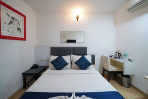 A hotel room with a bed, bedside table, desk, chair, and a wall-mounted mirror. - VH Hotels Domlur (Bengaluru)