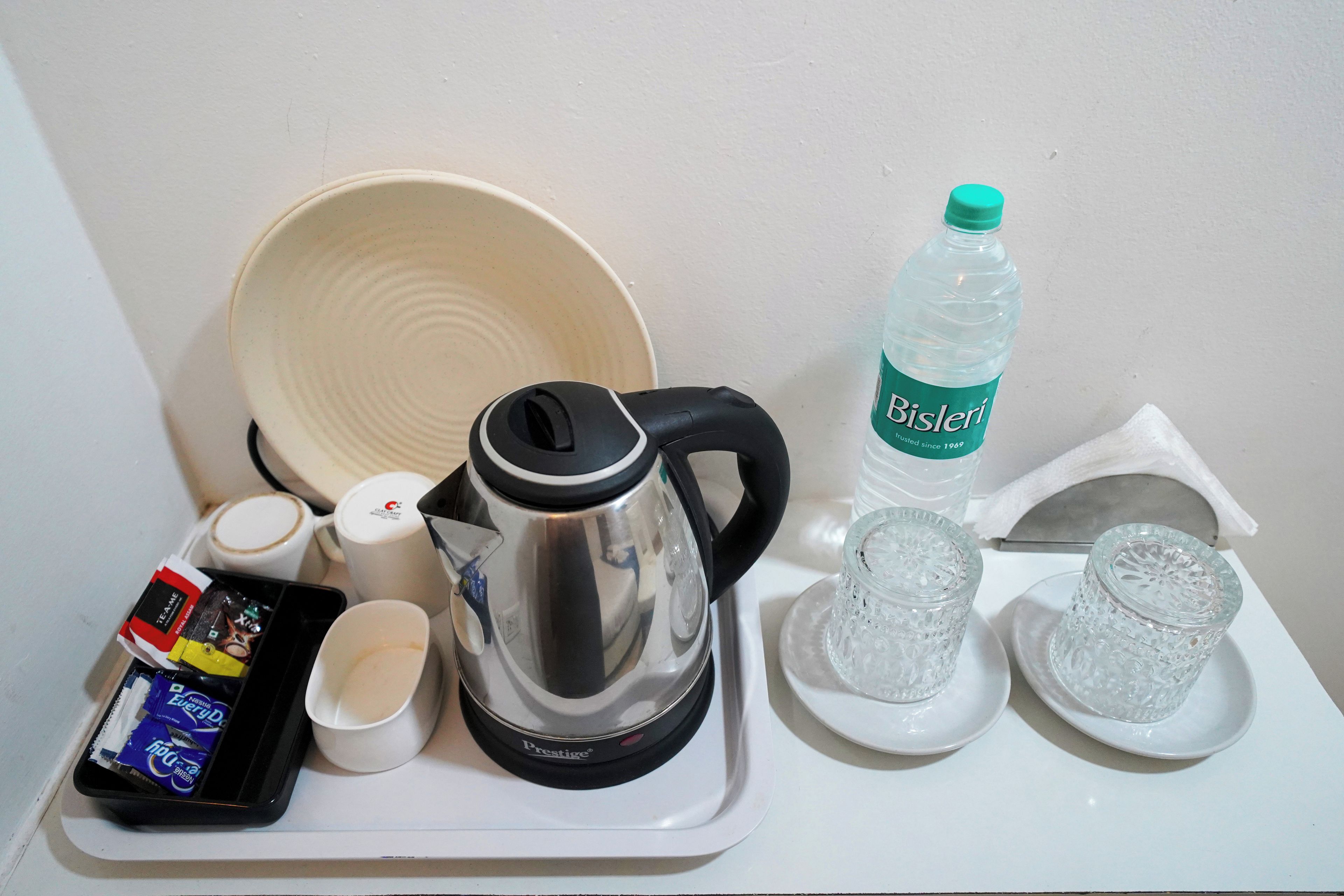 A tray with a coffee maker, a bottle of water, two cups, a bowl, and some snacks.