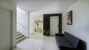 A modern interior with a staircase, a black sofa, and a door leading to a room with exercise equipment. - VH Hotels Domlur (Bengaluru)