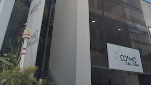 A modern building with a glass facade, a prominent entrance with a sign reading "COSMO ANNORA", and a visible staircase leading to an upper level. - VH Hotels Domlur (Bengaluru)