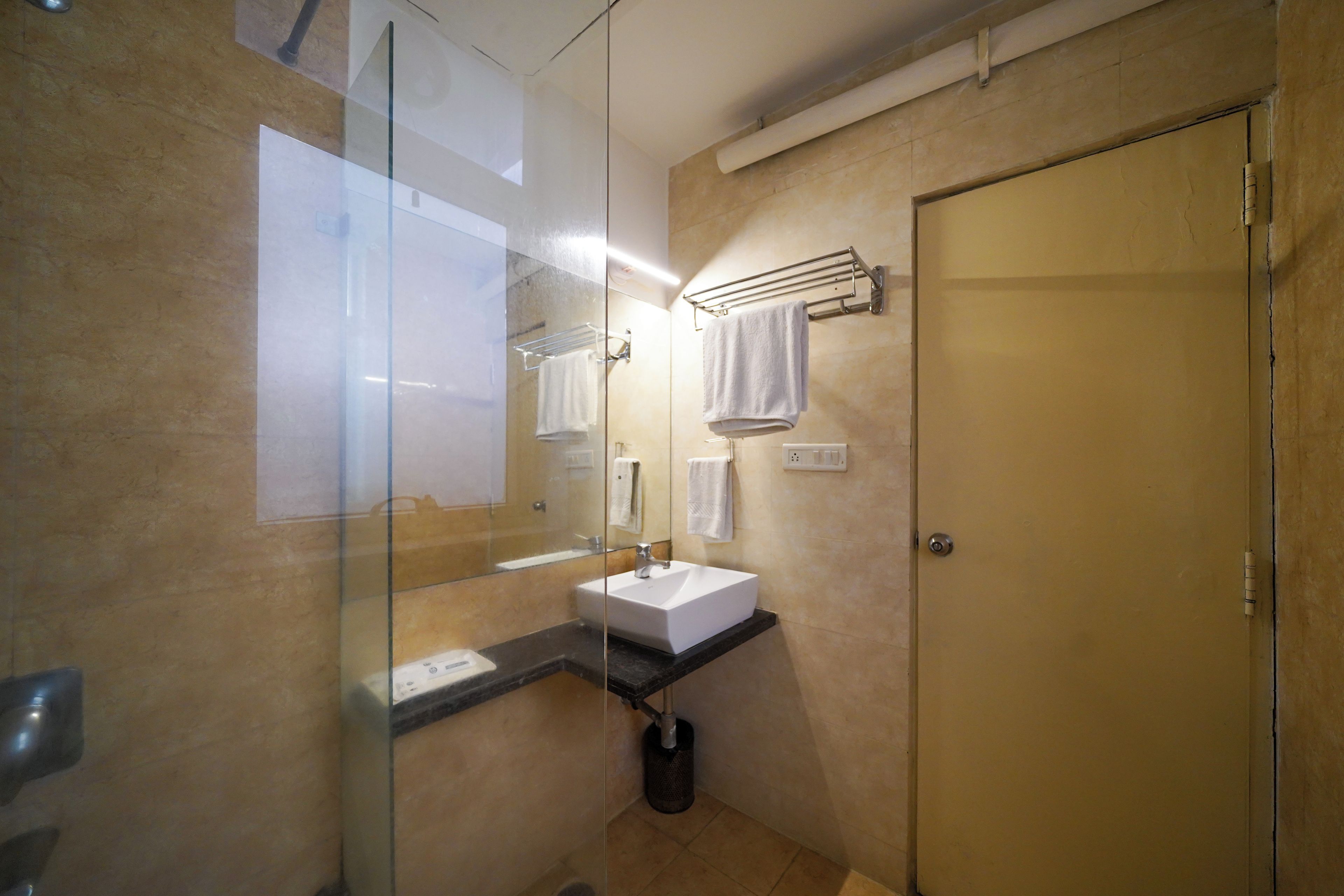 A bathroom with a glass shower enclosure, a white sink, and a towel rack.
