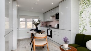 Een moderne keuken met witte kasten, een eethoek met een ronde tafel en stoelen, en een groene bank in een zithoek.