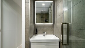 Een moderne badkamer met een wit wastafelmeubel, een spiegel en een douchecabine met glazen wanden.