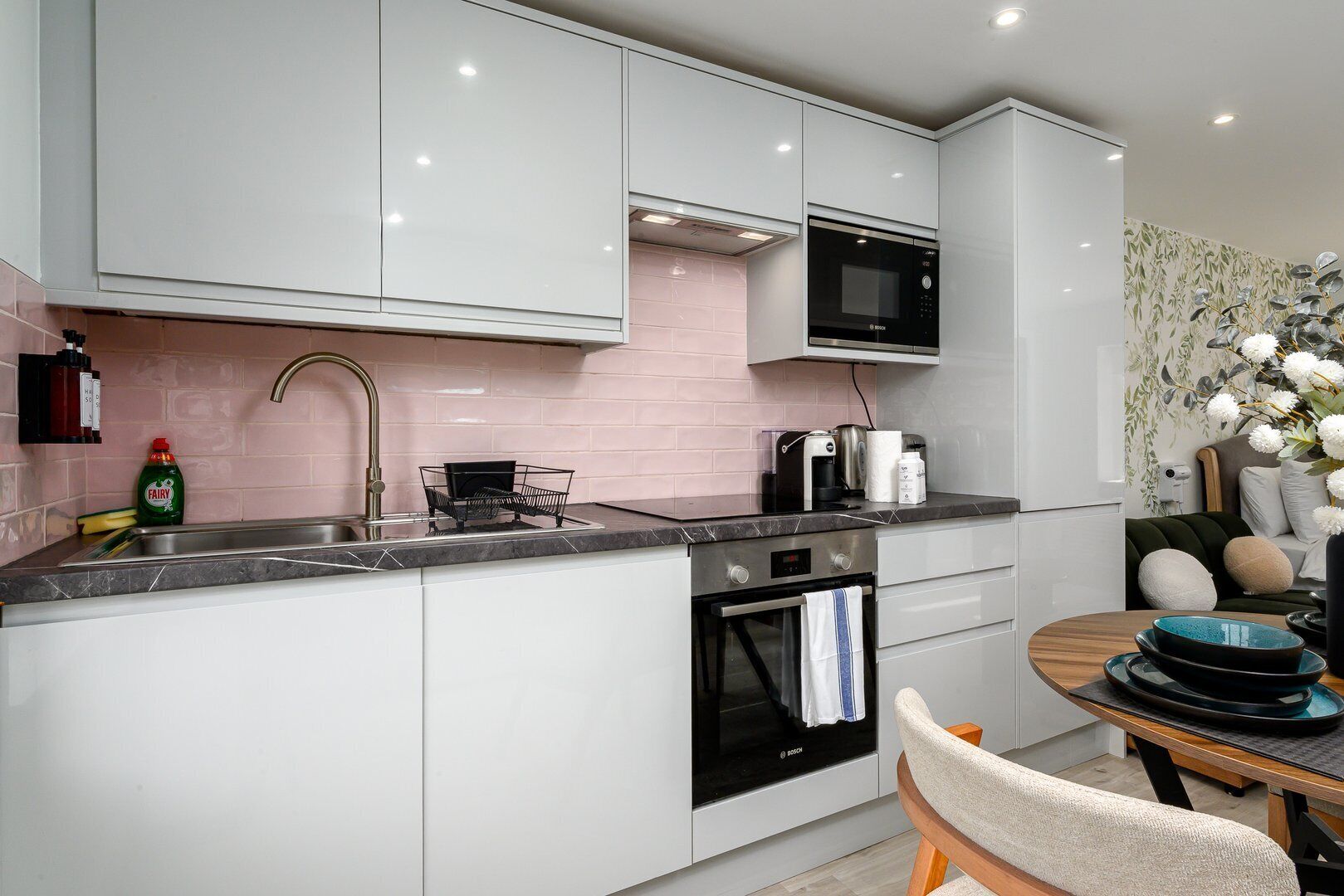 A modern kitchen with white cabinets, a Bosch oven, a microwave, and a sink with a dish rack.