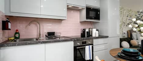A modern kitchen with white cabinets, a Bosch oven, a microwave, and a sink with a dish rack.