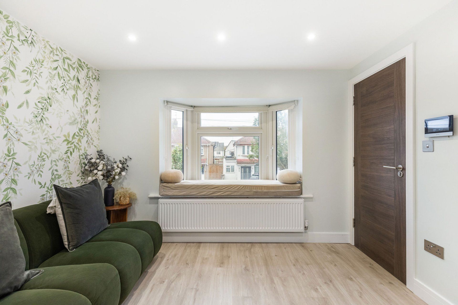 A room with a green sofa, a radiator, a bay window with a cushion, and a door with a lock.