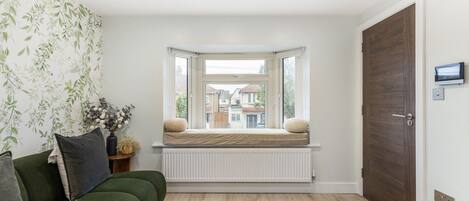 A room with a green sofa, a radiator, a bay window with a cushion, and a door with a lock.