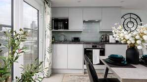 Een moderne keuken met witte kasten, een Bosch magnetron en een zwart fornuis. Er is een eethoek met een zwarte stoel en een vaas met witte bloemen.