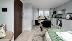 Een moderne keuken met witte kastjes, een eethoek met tafel en stoelen, en een groot raam met uitzicht op de stad.