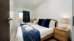Una camera d'albergo con due letti, un comodino in legno, una lampada e una finestra con tende.