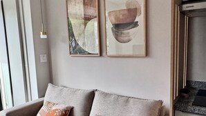 A modern living room with a grey sofa, two cushions, and two abstract paintings on the wall. - Cozy apartment in the heart of Pinheiros. (São Paulo)