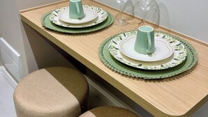 A small dining area with two stools, a table with a green placemat, and a wine glass. - Cozy apartment in the heart of Pinheiros. (São Paulo)