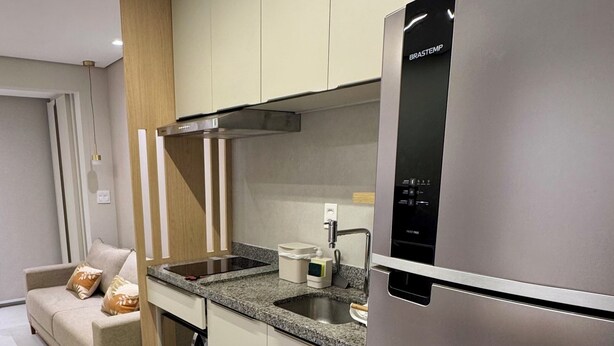 A modern kitchen with stainless steel appliances, light-colored cabinetry, and a built-in oven. - Cozy apartment in the heart of Pinheiros. (São Paulo)