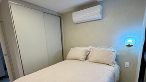 A bedroom with a bed, a wall-mounted air conditioner, and a bedside light. - Cozy apartment in the heart of Pinheiros. (São Paulo)