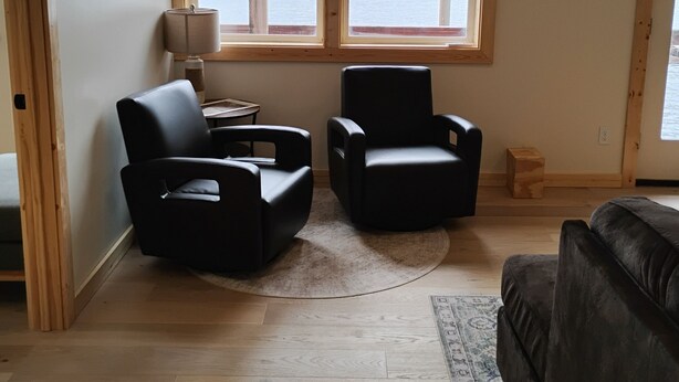 A room with two black leather chairs, a small side table with a lamp, and a large window offering a view of mountains and water.