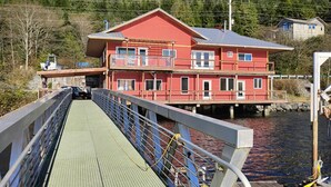 A red two-story house with a balcony, located by a body of water.