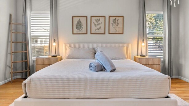 A bedroom with a large bed, two bedside tables, a ladder, and three framed botanical prints on the wall. - Spacious 3BR w Parking Pet Friendly (Austin)