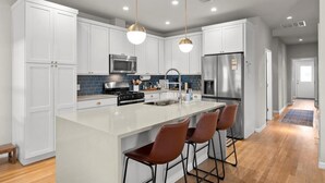 A modern kitchen with white cabinets, stainless steel appliances, a large island with bar stools, and pendant lighting. - Spacious 3BR w Parking Pet Friendly (Austin)