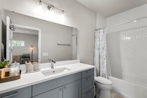 A modern bathroom with a white sink, grey cabinets, a large mirror, and a shower curtain. - Spacious 3BR w Parking Pet Friendly (Austin)