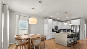 A modern kitchen with white cabinets, a central island with bar stools, a dining area with a round table and chairs, and pendant lighting. - Spacious 3BR w Parking Pet Friendly (Austin)