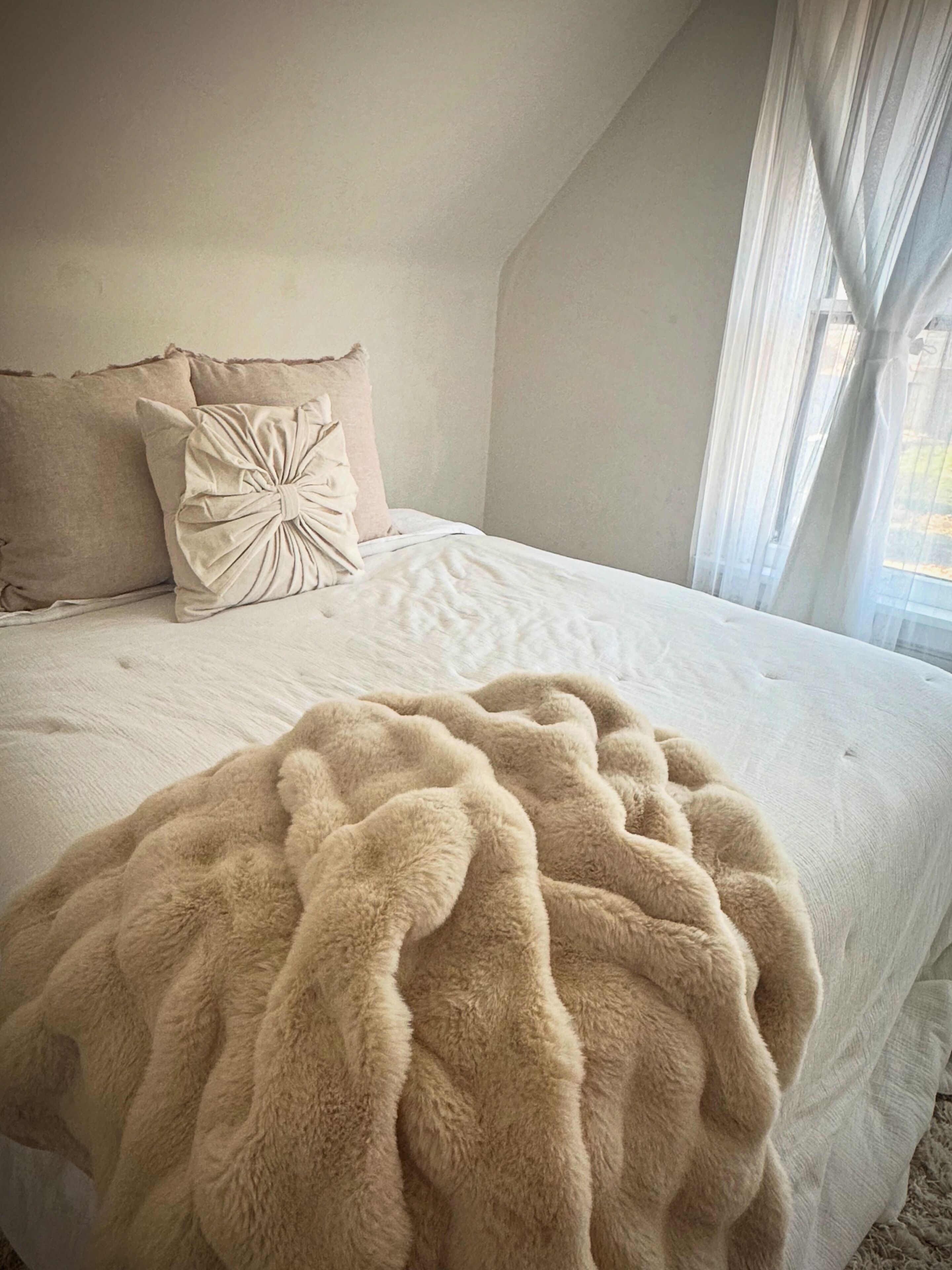 Ein Schlafzimmer mit einem großen Bett, einer flauschigen, beigefarbenen Decke und zwei Kissen.
