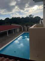 Una piscina con una estructura de techo rojo y vistas a árboles y un cielo nublado.