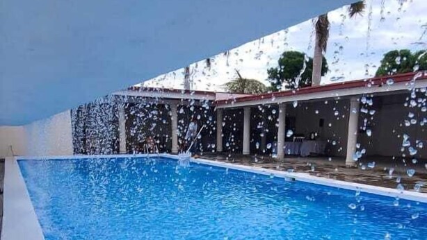 A swimming pool with clear blue water, surrounded by a covered area with columns and a roof.