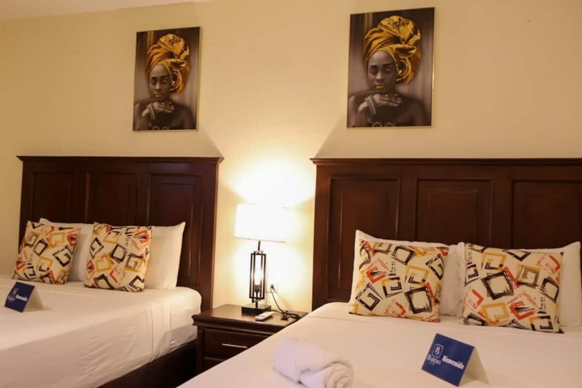 Een hotelkamer met twee bedden, elk voorzien van gestreepte kussens en een nachtkastje met een lamp.