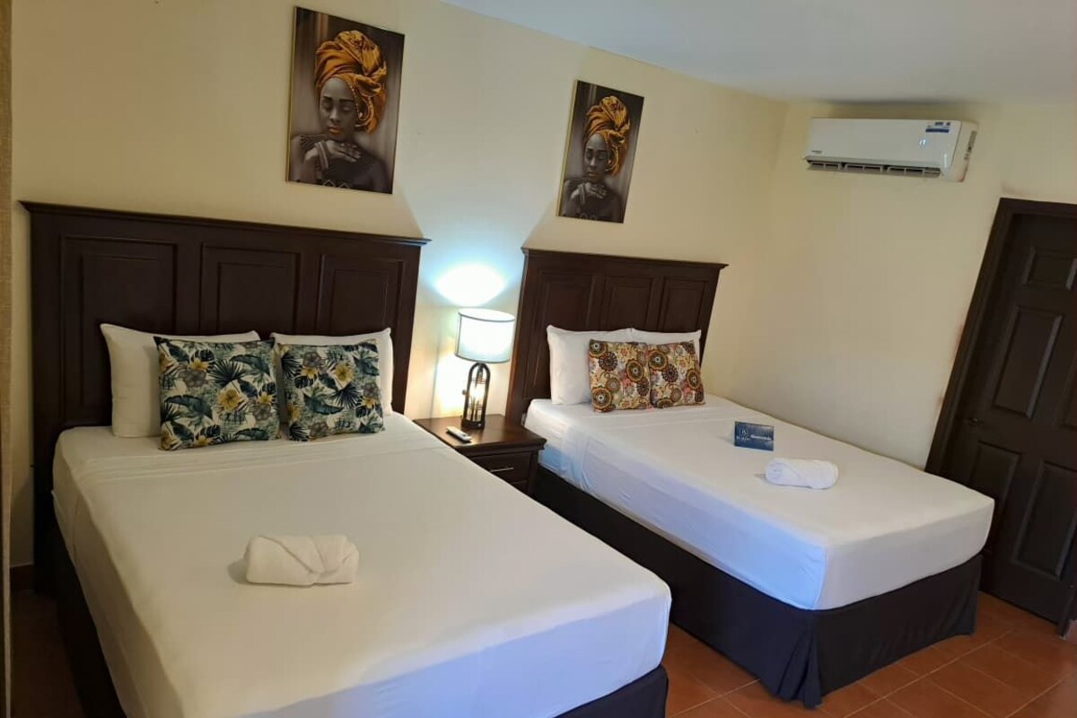 Two single beds with headboards, a nightstand, a lamp, and an air conditioning unit.