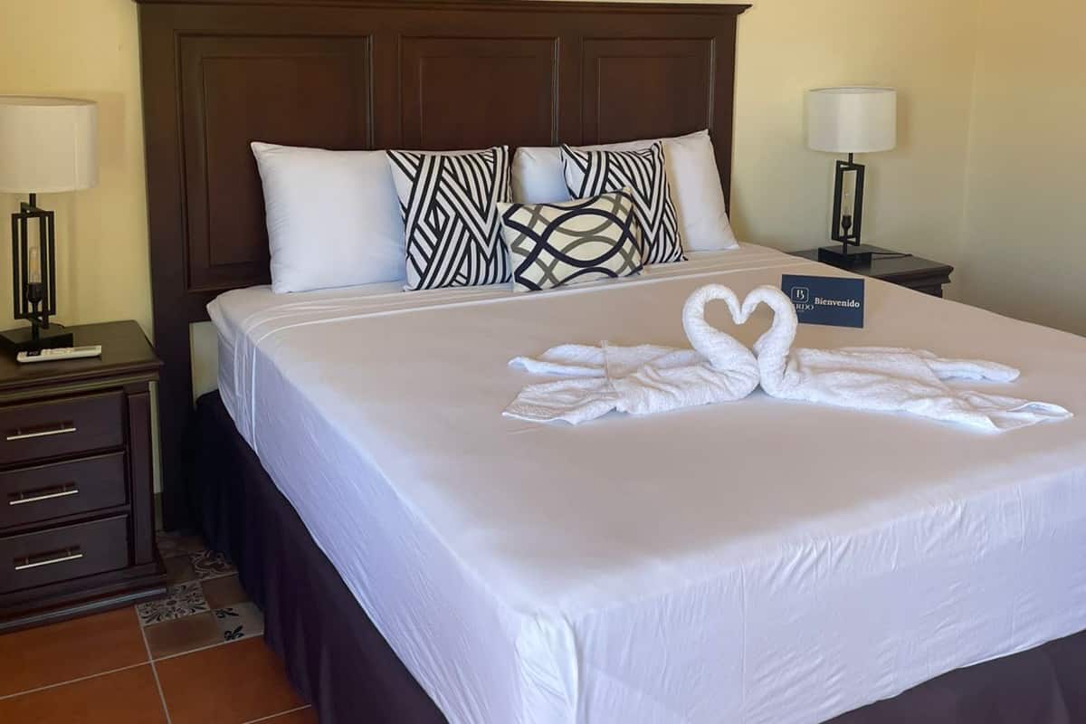 Een net opgemaakt bed met witte lakens, twee bijpassende kussens en een handdoek gevouwen in de vorm van een zwaan.