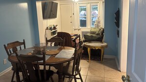 Un comedor con una mesa y sillas de madera, un televisor montado en la pared y un ventanal con cortinas.