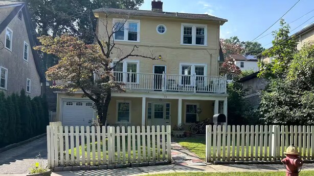 Una casa de dos pisos con valla de piquete blanca, un hidrante y un césped bien cuidado.