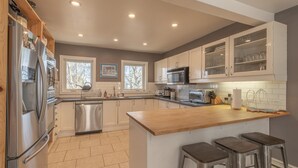 A modern kitchen with stainless steel appliances, a wooden island with bar stools, and large windows.