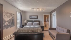 A bedroom with a large bed, a nightstand, a lamp, a framed picture on the wall, and a window with a view of a canal.