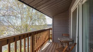 A wooden deck with a table and chairs, overlooking a tree-lined area.