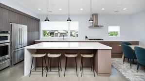 A modern kitchen with a large island, bar stools, stainless steel appliances, and pendant lighting.