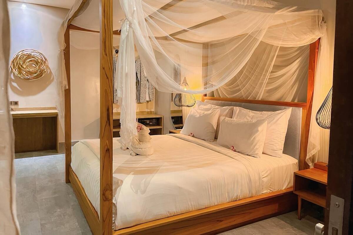 Ein Himmelbett mit weißer Bettwäsche, Holzrahmen und einem kleinen Nachttisch mit Lampe.