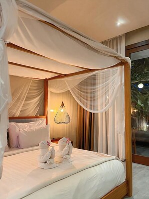 A four-poster bed with white linens and a canopy, a bedside table with a lamp, and a view of greenery through a window. - The Moonci (Ubud)