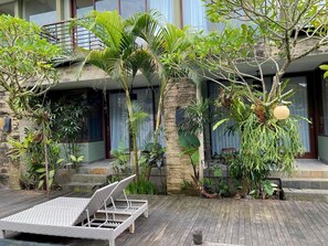 A modern outdoor area with a wooden deck, lounge chairs, and various tropical plants. - The Moonci (Ubud)