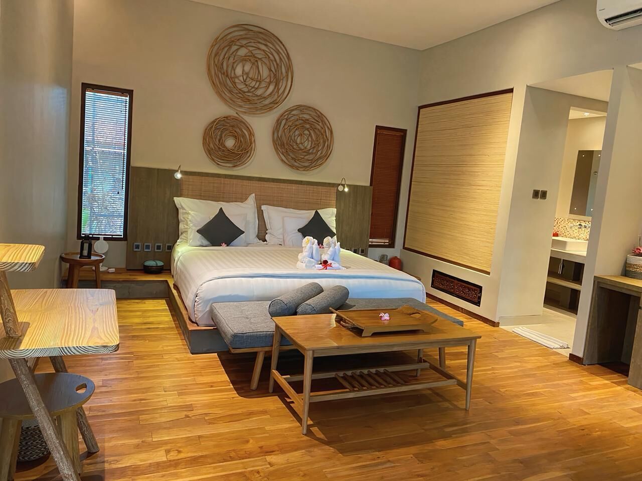Una habitación de hotel moderna con una cama grande, piso de madera, un escritorio y una mesita.