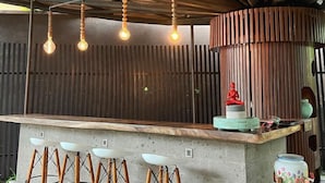 Una zona de bar rústica con mostrador de hormigón, taburetes de madera y lámparas colgantes.