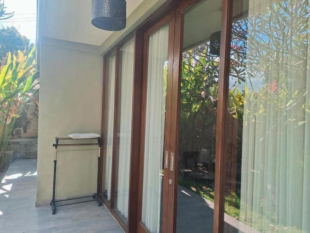 A room with a sliding glass door, a small table with a cushion, and a view of greenery outside.