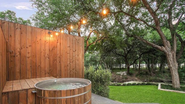 A wooden spa area with a hot tub, surrounded by a well-maintained lawn and trees. - South Lamar Luxe Creekside Hot Tub (Austin)