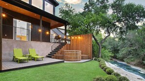 A modern house with a wooden deck, outdoor seating, and a view of a river. - South Lamar Luxe Creekside Hot Tub (Austin)