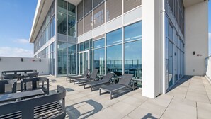 A rooftop terrace with sun loungers, a table, and chairs, overlooking a cityscape.