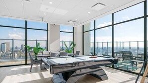 A modern indoor pool table with a city view, large windows, and a high ceiling.
